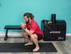 Dr. john holding a dumbbell close to his chest squatting down in a goblet squat to help strengthen his lower back